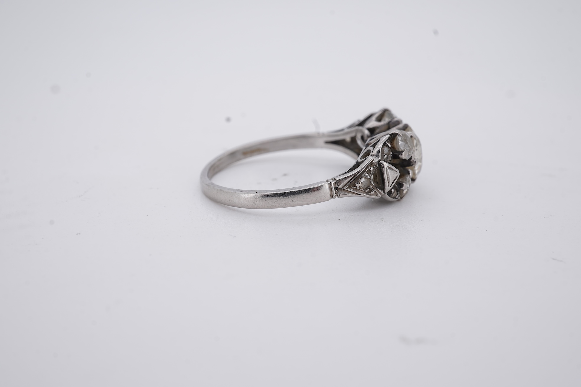 A white metal (stamped platin) and single stone diamond ring, flanked by four smaller diamonds and rose cut diamond chip set shoulders, size P, gross weight 3.8 grams.